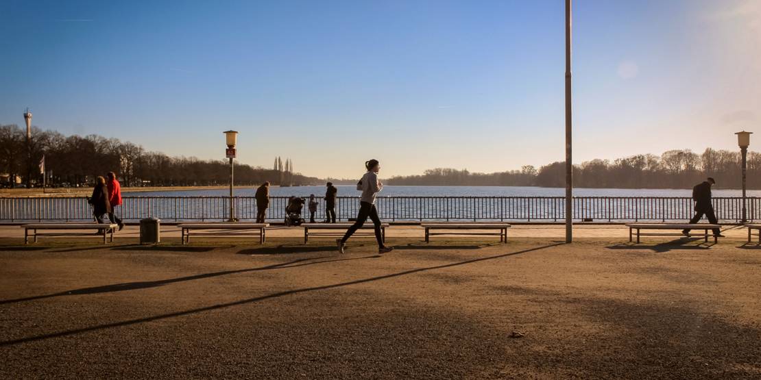 Eine Joggerin und fünf weitere Personen vor dem Gitter des Maschsee-Nordufers.